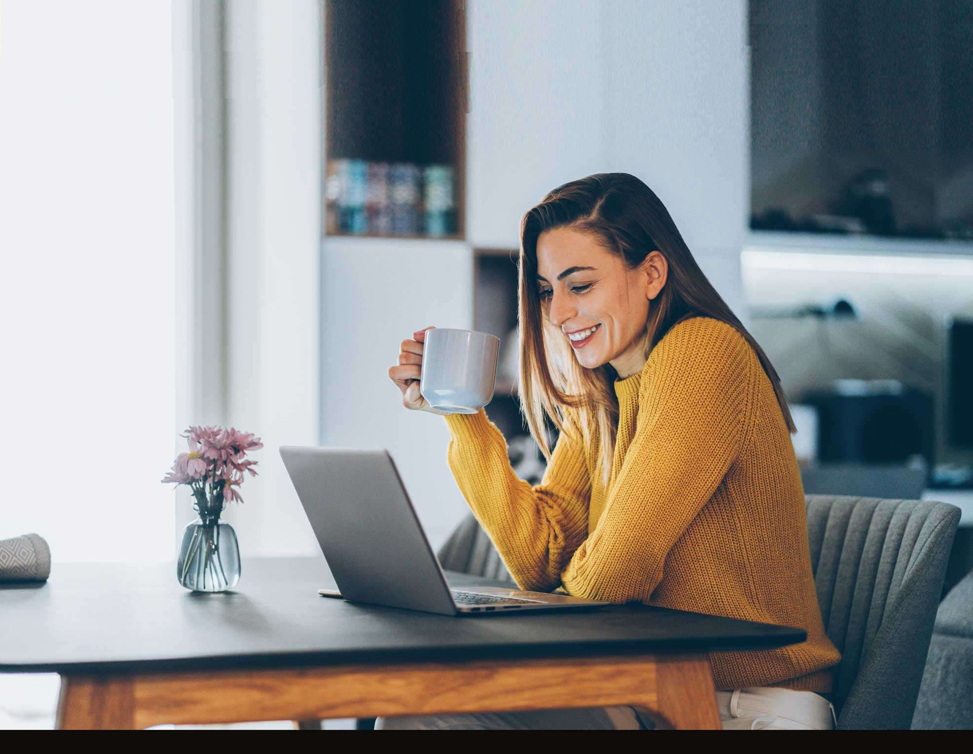 Woman sitting behind computer smiling with a mug