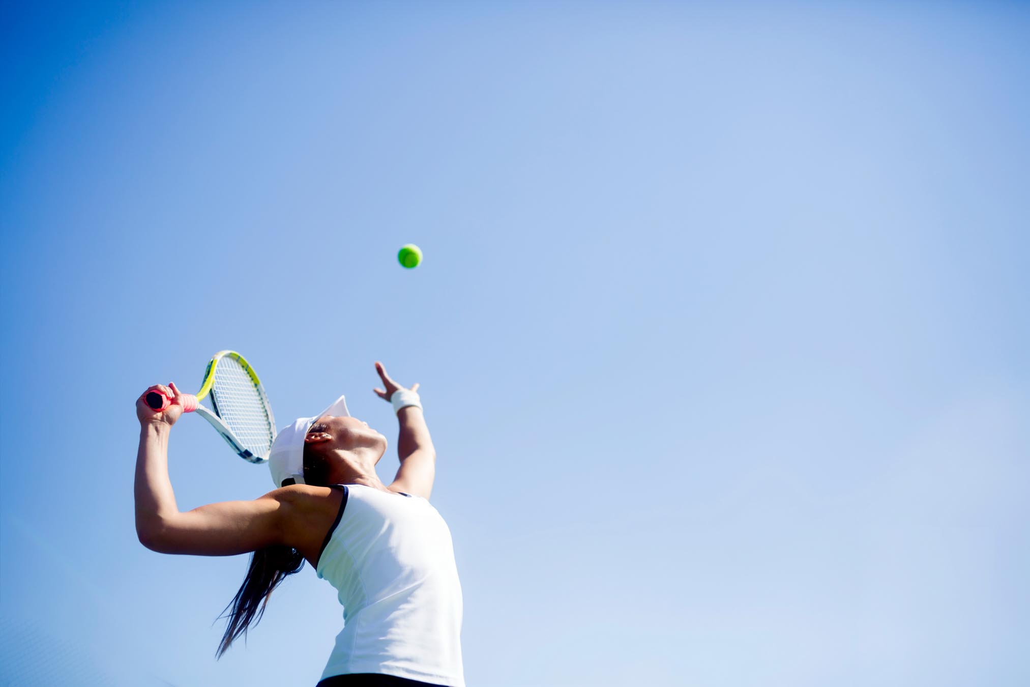Woman holding tennis racket and aiming at tennis ball in the air